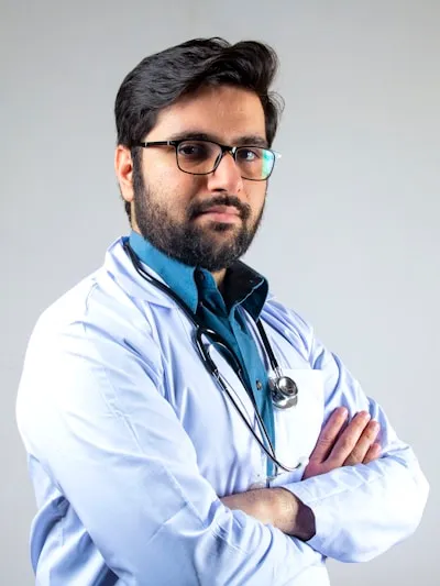 Doctor wearing a mask and glasses looking directly at the camera in a professional clinical setting, with colors and contrast optimized to remain clear and visually appealing in both light and dark mode