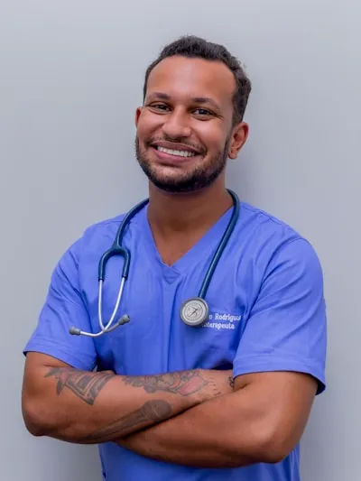 A confident male dentist in a modern dental clinic, smiling gently, with dental chair and equipment in the background, bright and professional lighting, with colors and contrast optimized to remain clear and visually appealing in both light and dark mode